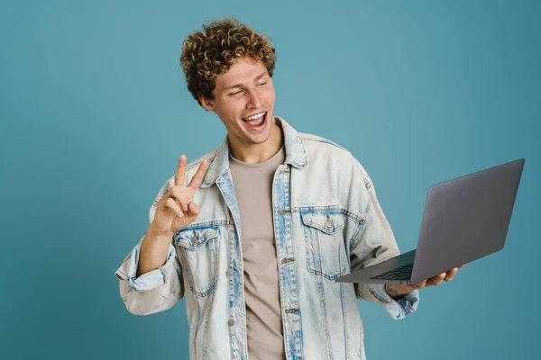 Молодий Збуджений Чоловік Використовує Ноутбук Показуючи Знак Миру Ізольований Синьому — стокове фото