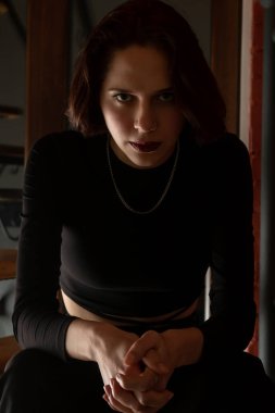 Koyu dudaklı esmer kızın dramatik portresi merdivenlerde oturuyor.