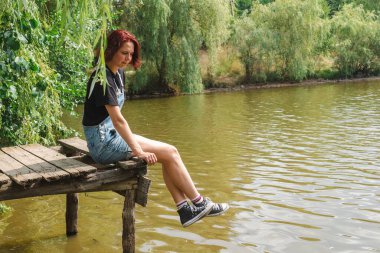 Kısa saçlı genç kız eski tahta bir piercingin üzerinde oturuyor..