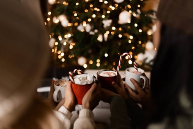 Woman holds a winter cup close up. Woman hands with elegant french manicure nails design holding a cozy knitted mug with cocoa, tea or coffee and a candy cane. Winter and Christmas time concept.