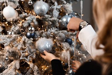 close-up of the hands of a man and a woman decorating a christmas tree with balls