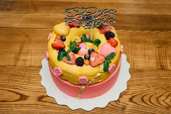 bright multi-colored cake with fruits and the inscription Happy Birthday in Russian. Close-up with selected focus point