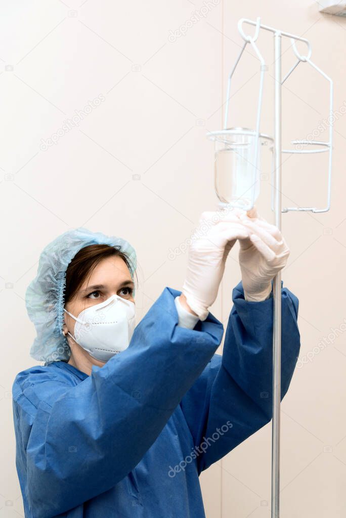 doctor girl in a mask, gown and gloves sets up a drip