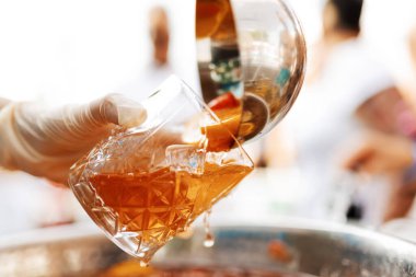 close-up of the bartender's hands pouring a cold cocktail with ice into a glass