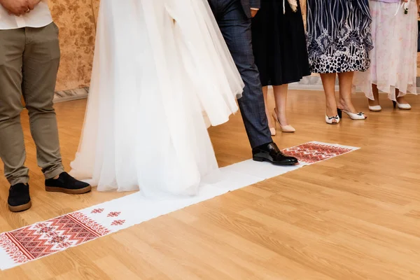 The bride and groom stand on an embroidered towel with the inscription for luck and fate in Ukrainian during a church wedding.
