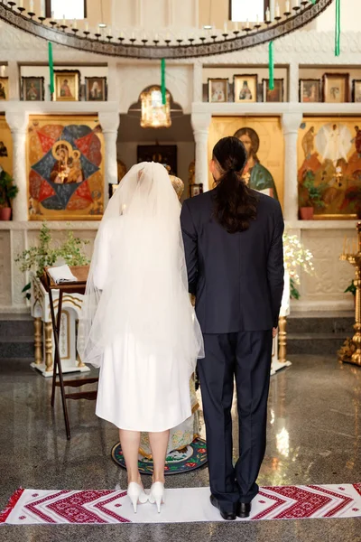 The bride and groom stand on an embroidered towel during a church wedding.