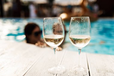 Two glasses of sparkling champagne or prosecco on a white wooden table next to the swimming pool in summer.