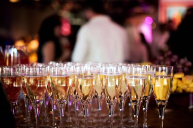 a lot of glasses with champagne on the background of blurred people