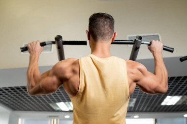 Sporcu kaslı erkek model spor salonunda yatay çubuğa yanaşıyor.