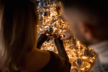 close-up of the hands of a man and a woman decorate the Christmas tree with balls