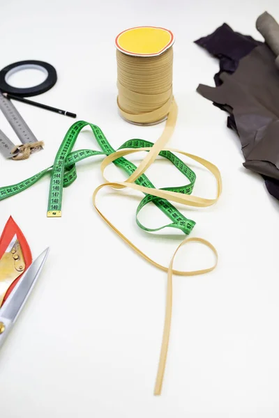 seamstress tools: pieces of fabric and fur, scissors, rulers, meter and pencil on a white table