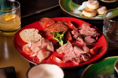 Kırmızı tabakta dilimlenmiş sosis, jambon ve pastırma.