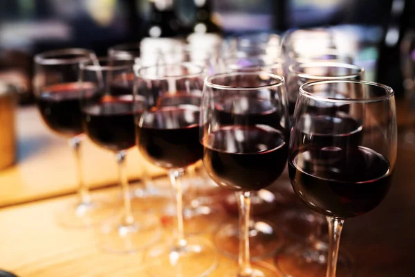 アルコールボトルの列を背景にバーに赤ワインとエレガントなワイングラスの行 — ストック写真
