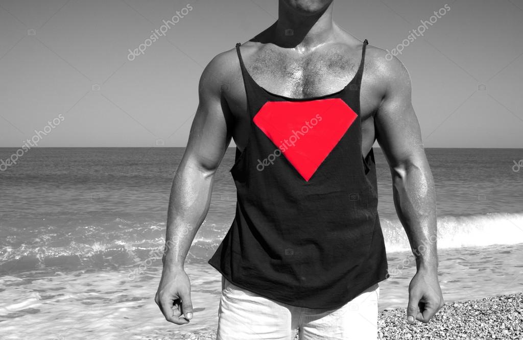 Muscular brutal man on the beach in a T-shirt with the logo of Superman