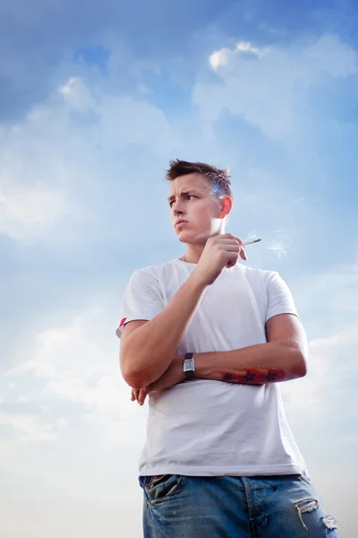 Un joven fumando cigarrillo sobre fondo azul del cielo —  Fotos de Stock