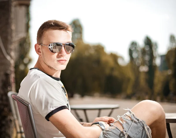 Casual ragazzo in sunglass seduta su panchina — Foto Stock
