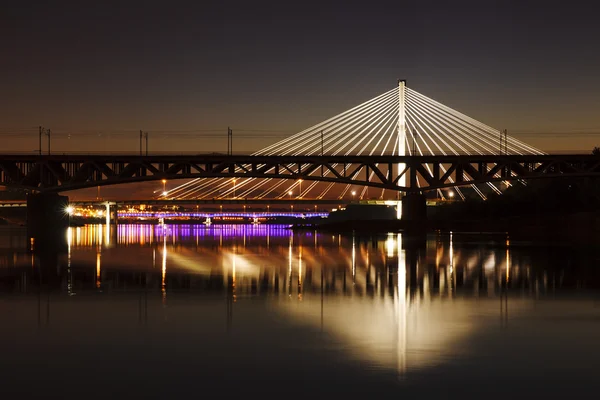 Nachts beleuchtete Brücke, die sich im Wasser spiegelt — Stockfoto