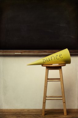 Yellow dunce hat on stool with chalkboard clipart