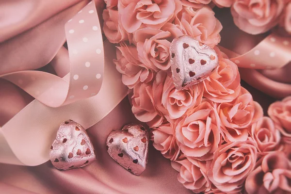 Hart gemaakt van roze rozen met linten en chocolade op satijn — Stockfoto