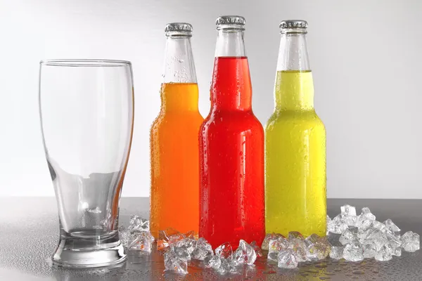 Three bottles with drinks with glass and ice — Stock Photo, Image