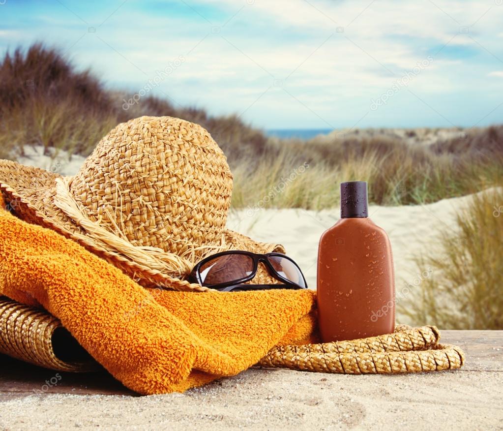 Straw hat with towel and lotion at the beach 