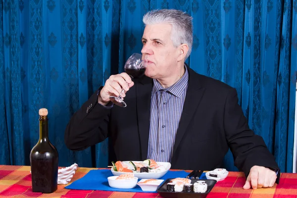 Человек ест суши и пьет красное вино — стоковое фото