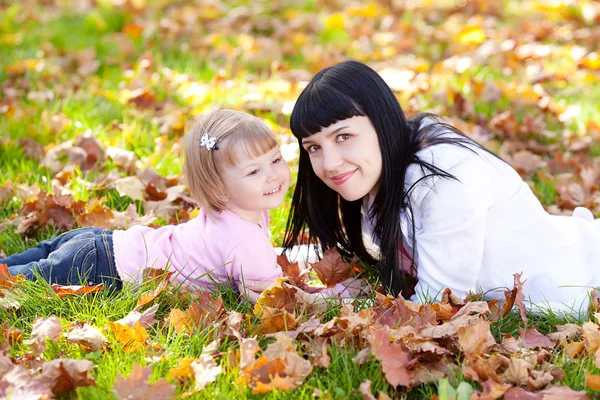 Vacker ung mamma och hennes dotter liggande på hösten lämn — Stockfoto