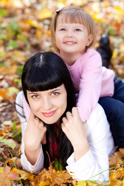 Schöne junge Mutter und ihre Tochter auf dem Herbstblatt liegend — Stockfoto