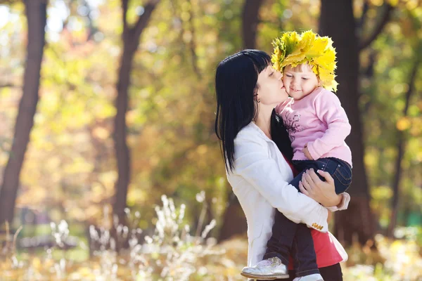 Vacker ung mamma håller sin dotter i en krans av lönn — Stockfoto