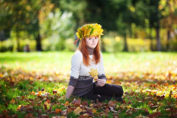 Young redhead teenager woman in a wreath of maple leaves sitting — Stock Photo, Image