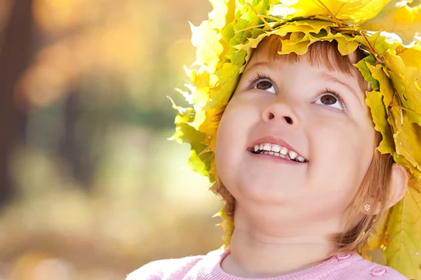 Hermosa niña en una corona de hojas de arce en otoño — Foto de Stock