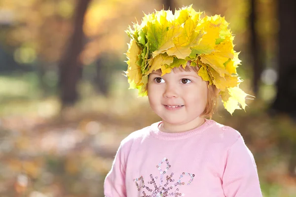 Beautiful little girl in a wreath of maple leaves in autumn fore — Stock Photo, Image