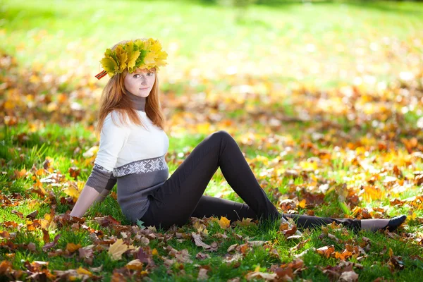 Joven pelirroja adolescente mujer en una corona de hojas de arce sentado — Foto de Stock