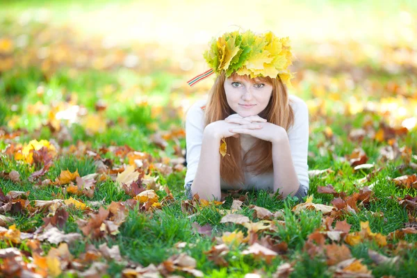 Young redhead teenager woman in a wreath of maple leaves lying o — Stock Photo, Image