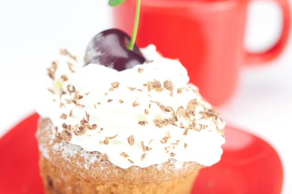 Muffin con crema batida, cerezas y taza roja sobre fondo blanco —  Fotos de Stock