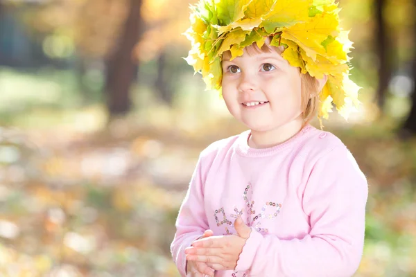 Vacker liten flicka i en krans av lönn lämnar hösten fore — Stockfoto