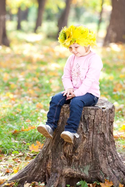 Beautiful little girl in a wreath of maple leaves sitting on stu — Stock Photo, Image