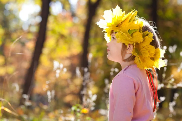 Hermosa niña en una corona de hojas de arce en otoño — Foto de Stock