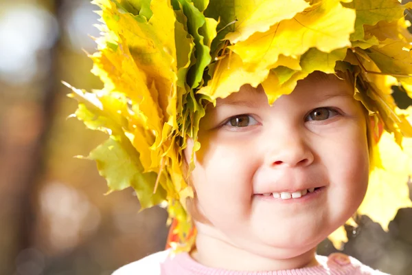 Vacker liten flicka i en krans av lönn lämnar hösten fore — Stockfoto