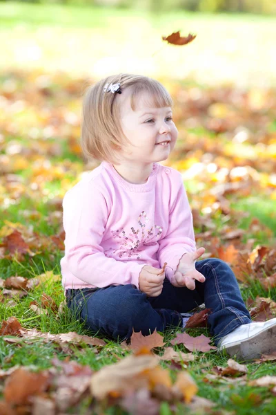 Linda menina sentada nas folhas de outono — Fotografia de Stock