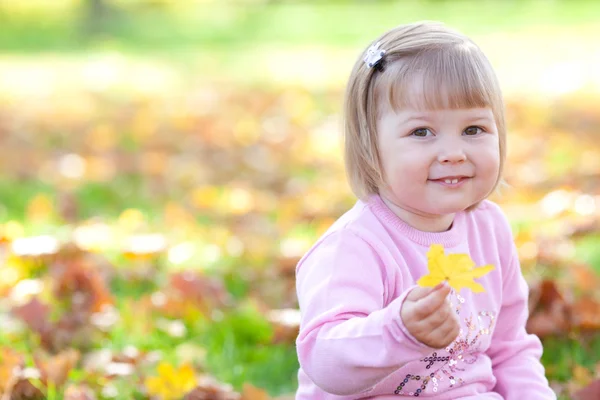 Hermosa niña sentada en las hojas de otoño — Foto de Stock