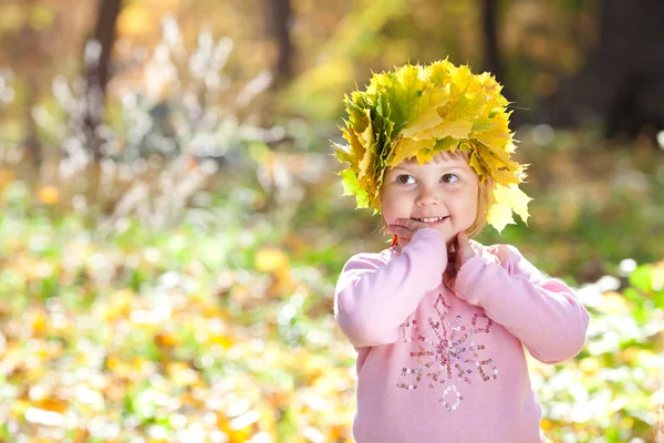 Vacker liten flicka i en krans av lönn lämnar hösten fore — Stockfoto