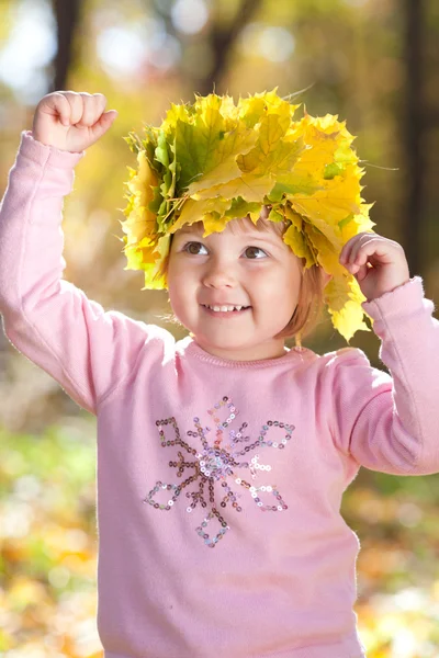 Beautiful little girl in a wreath of maple leaves in autumn fore — Stock Photo, Image