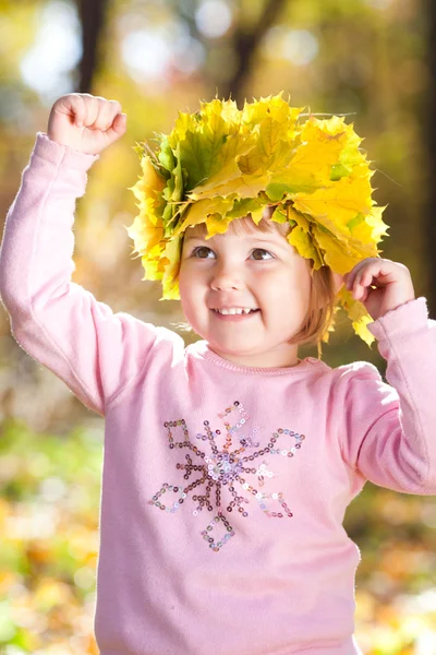 Hermosa niña en una corona de hojas de arce en otoño — Foto de Stock