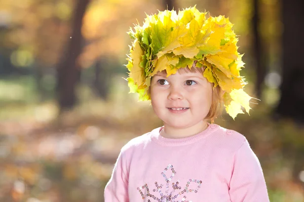 Linda menina em uma grinalda de folhas de bordo na frente outono — Fotografia de Stock