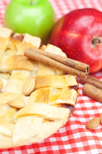 Apple pie, apples, cinnamon and almonds on plaid fabric — Stock Photo, Image