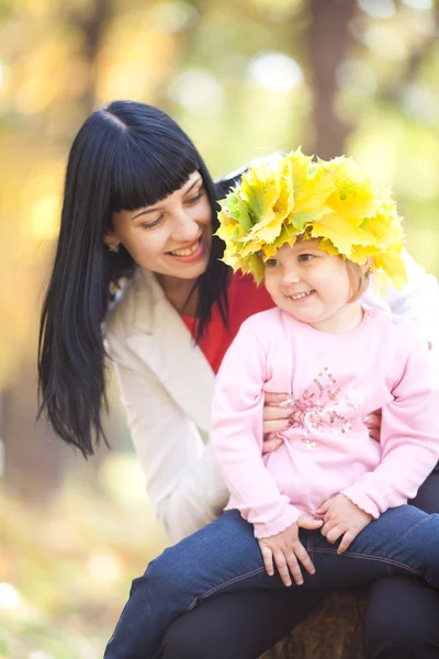 Schöne junge Mutter hält ihre Tochter in einem Kranz aus Ahorn — Stockfoto