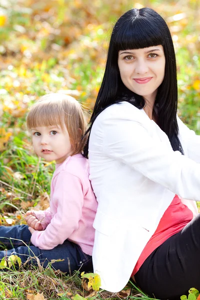 Beautiful young mother and her daughter sitting on the autumn le — Stock Photo, Image