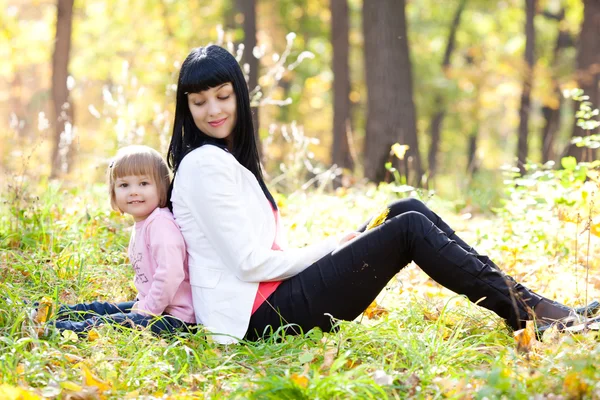 Vacker ung mamma och hennes dotter sitter i höst len — Stockfoto