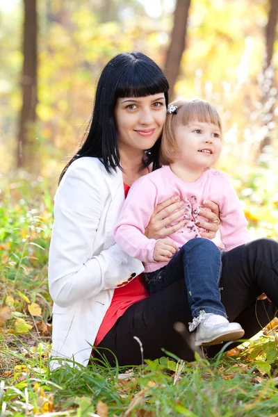 Vacker ung mamma och hennes dotter på autumv skogen — Stockfoto